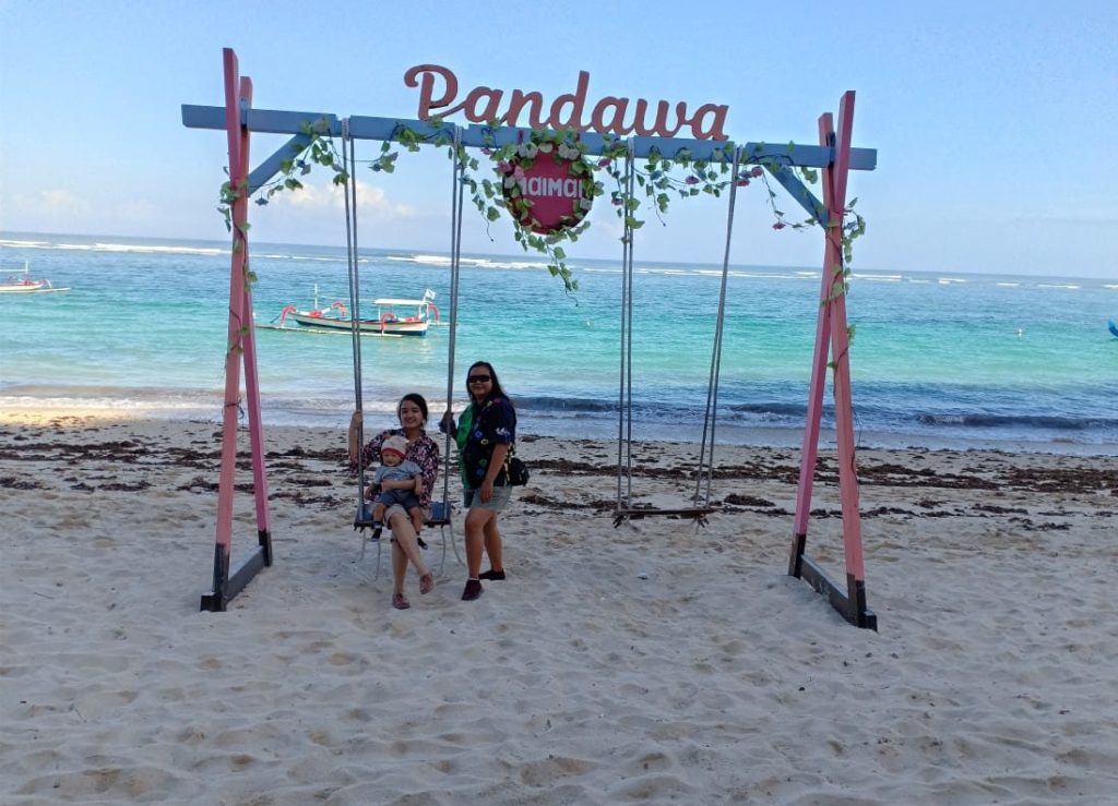 dua orang dan bayi di ayunan dekat pantai pandawa